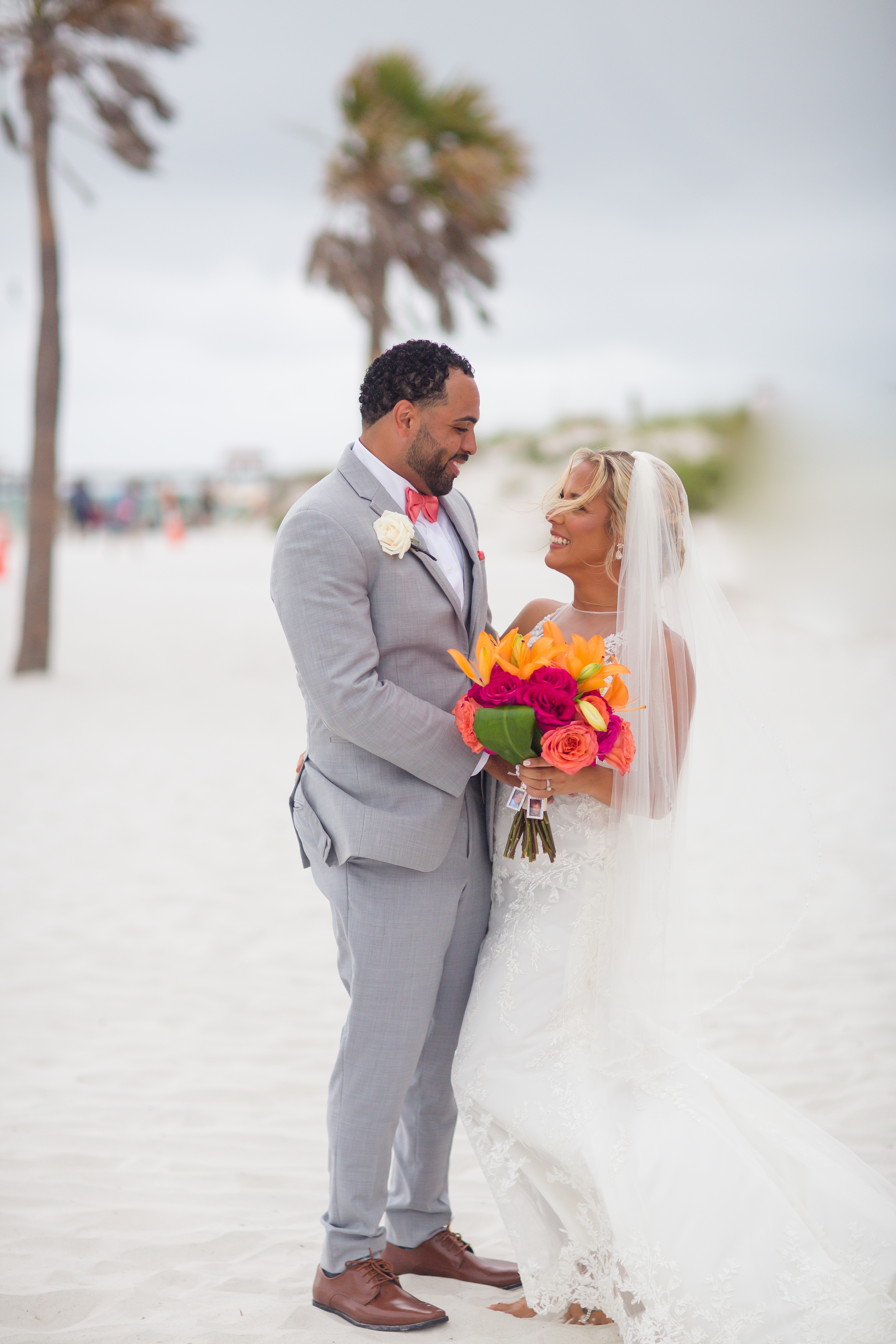 groom in gray suit with pink bowtie and bride in lace gown with colorful bouquet