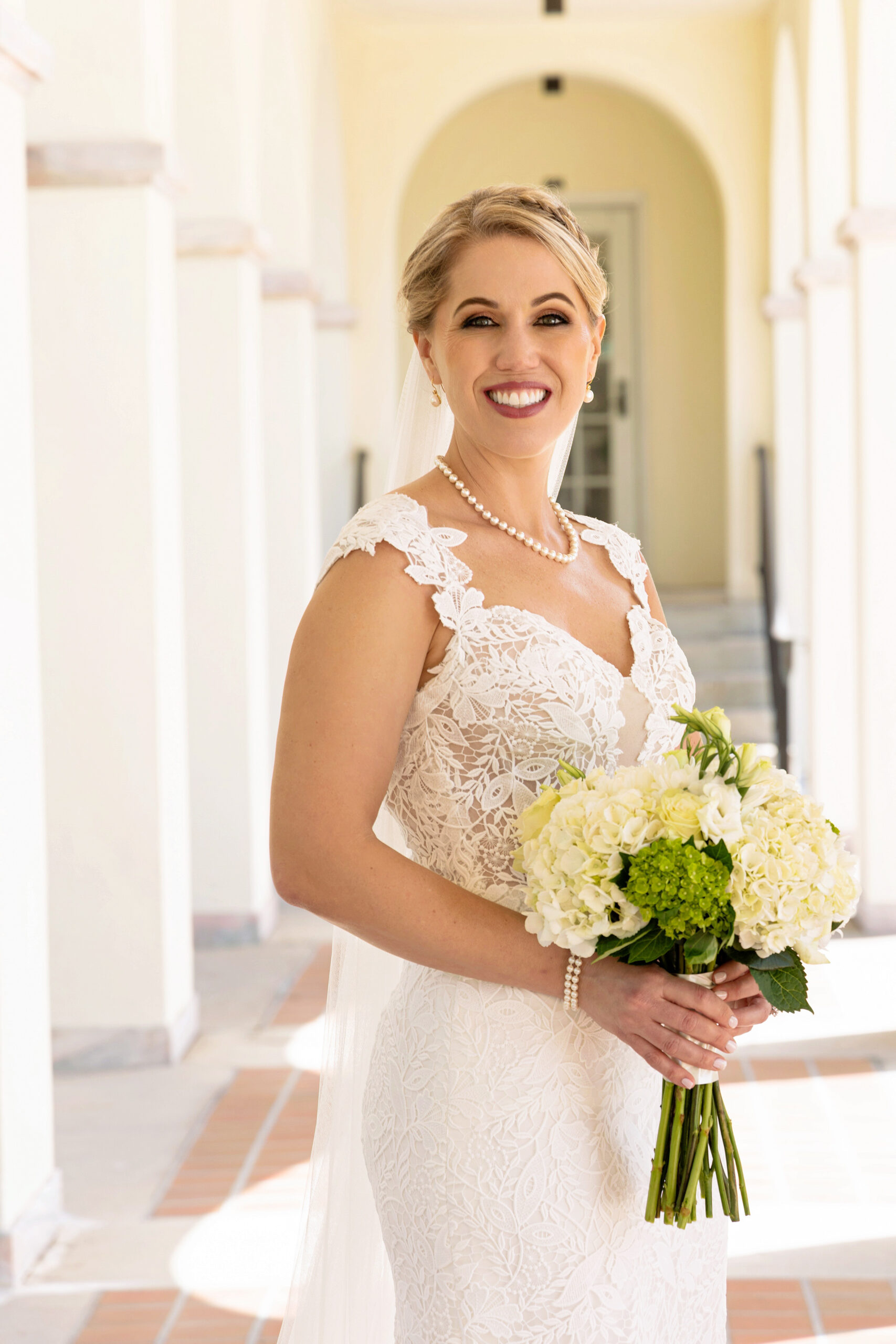 bride in fitting lace gown with pearl necklace and white and green bridal bouquet