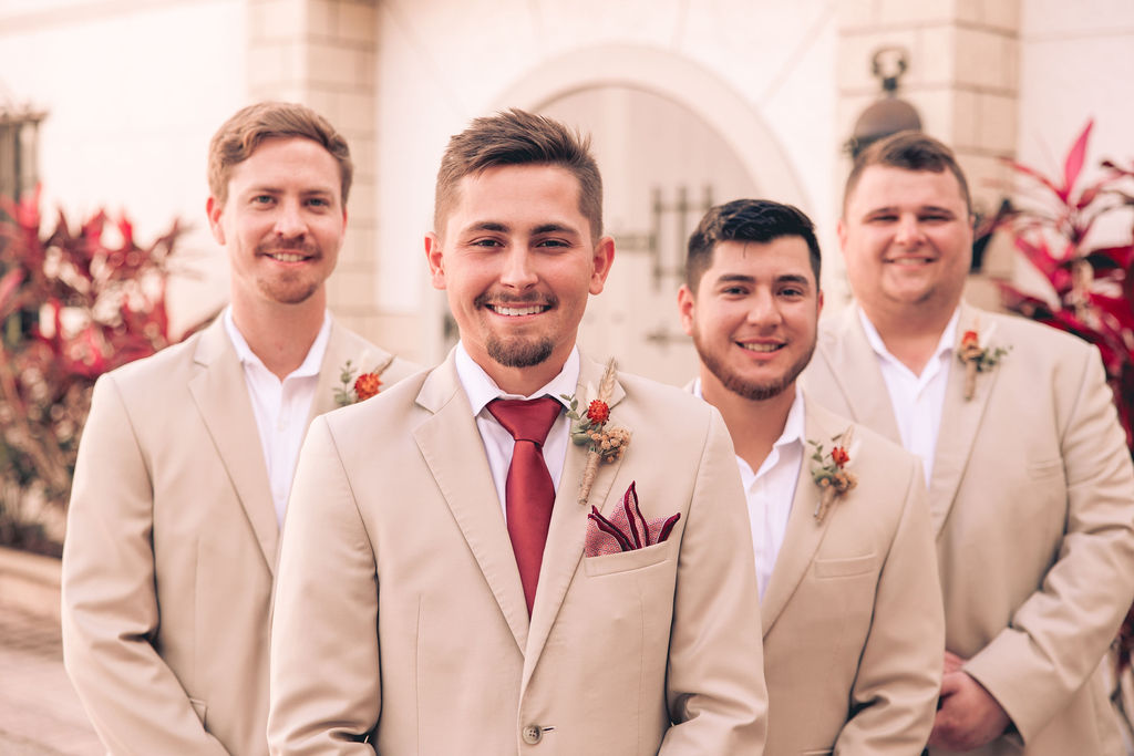 groomsmen in tan suits with red accessories