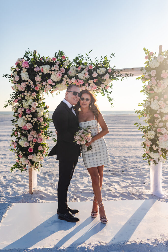 bride and groom by the coast under colorful floral arch