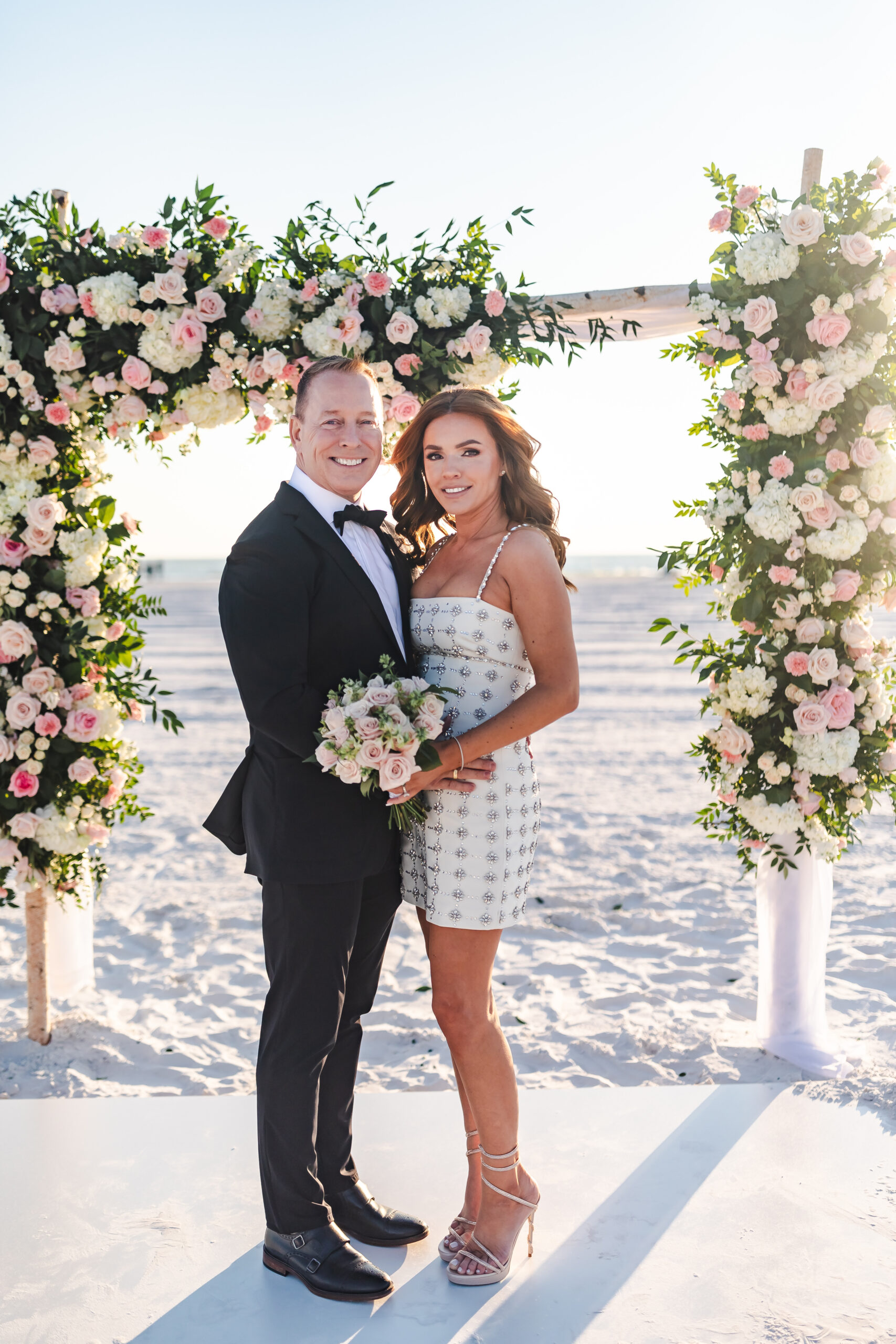 bride and groom under wedding ceremony arch covered in florals by Precious Moments Events