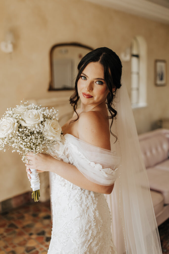 bride in off shoulder lace gown with bridal bouquet of white roses and baby's breath