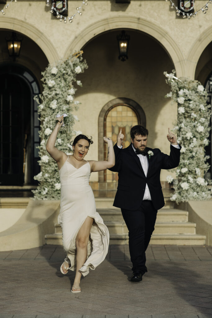 bride and groom under green and white wedding ceremony arch