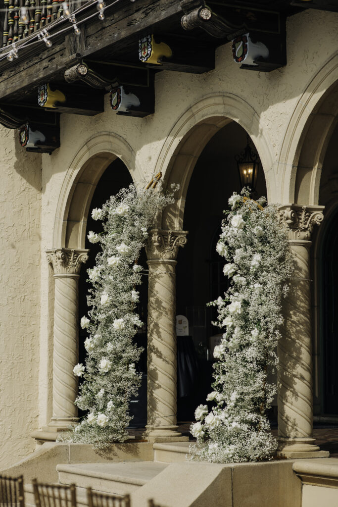 split wedding ceremony arch covered in greenery, white roses, and baby's breath