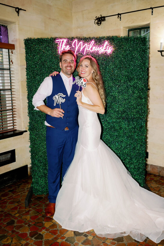 bride and groom with greenery decor wall