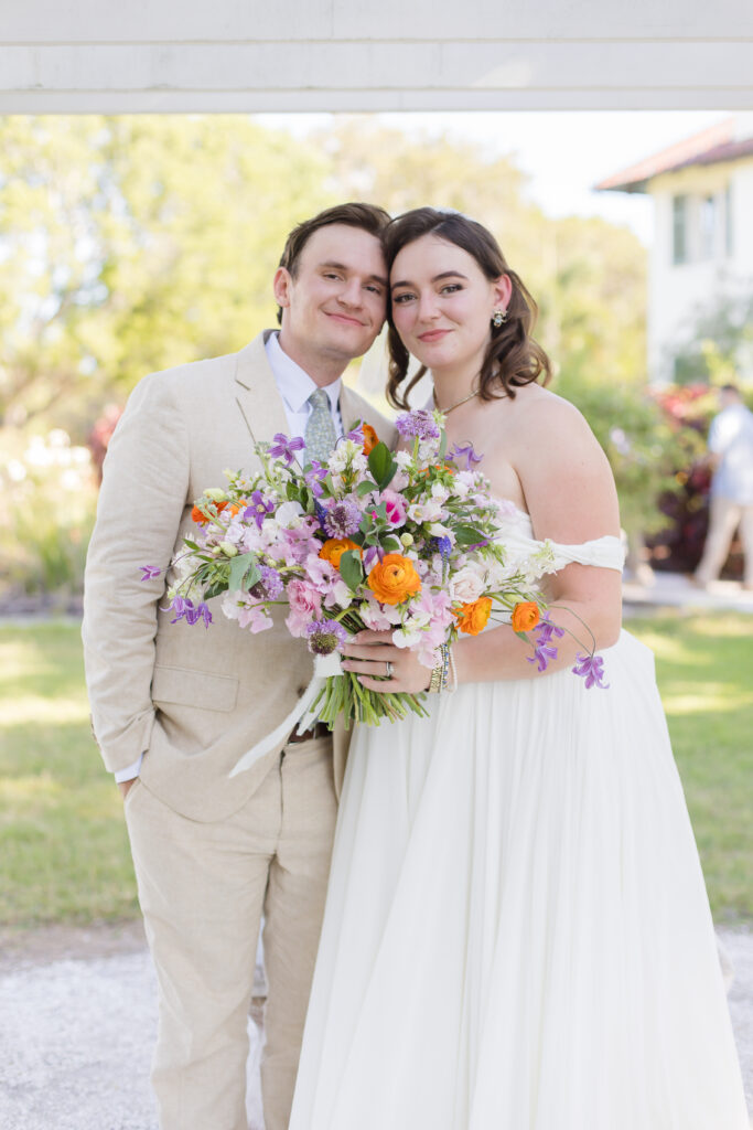 bride in lace and tulle gown with colorful floral bouquet and groom in tan suit