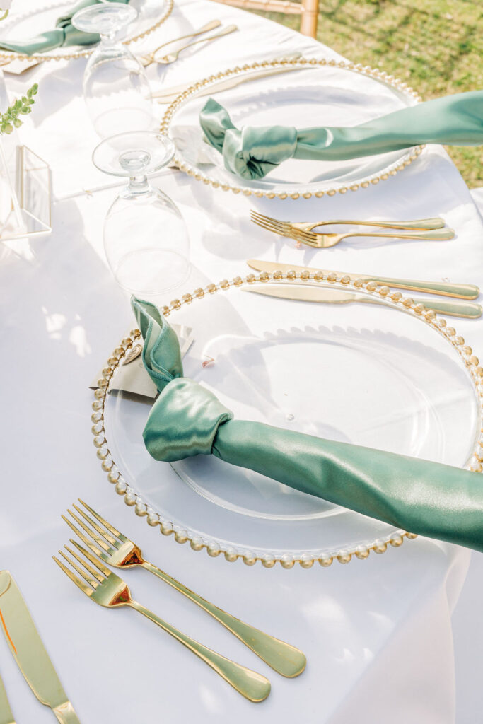 gold utensils and charger plate with green napkin on wedding tablescape