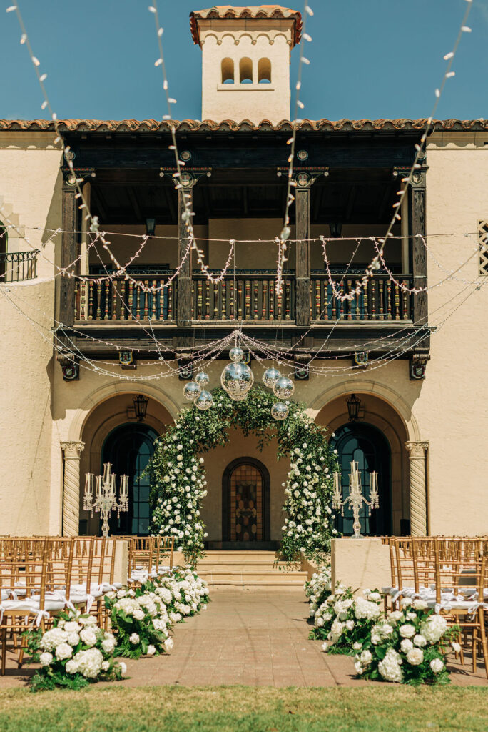 wedding ceremony at Powel Crosley Estate decorated with greenery, white roses, and stringed lights